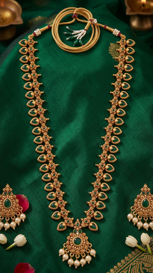 Flatlay of INNOVATE ART IMPEX gold-plated long temple necklace set with green stones and pearl drops resting on luxurious green silk fabric.