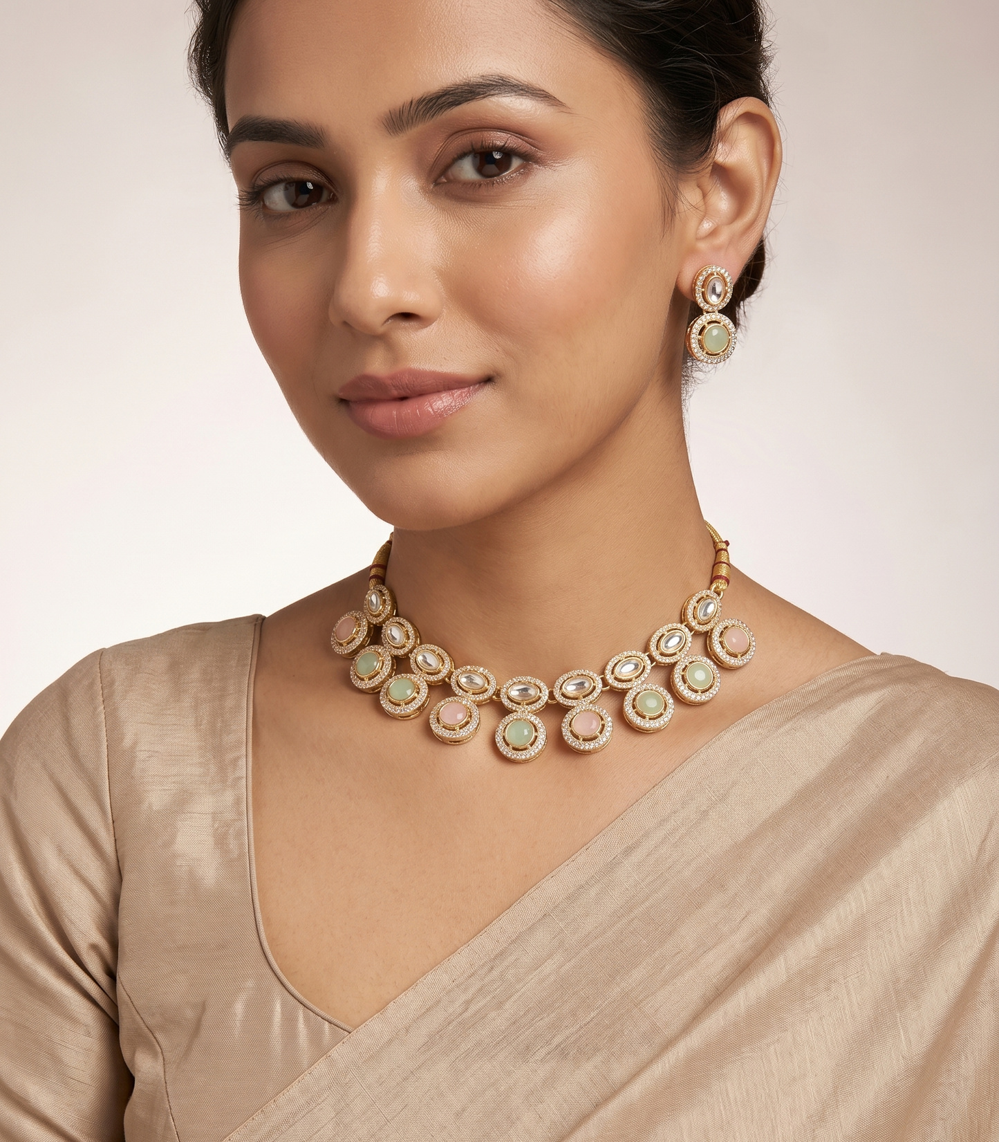 Woman wearing a gold necklace and earrings on a neutral background