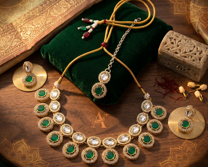 Ornate necklace with green gemstones on a wooden surface with a brand logo.
