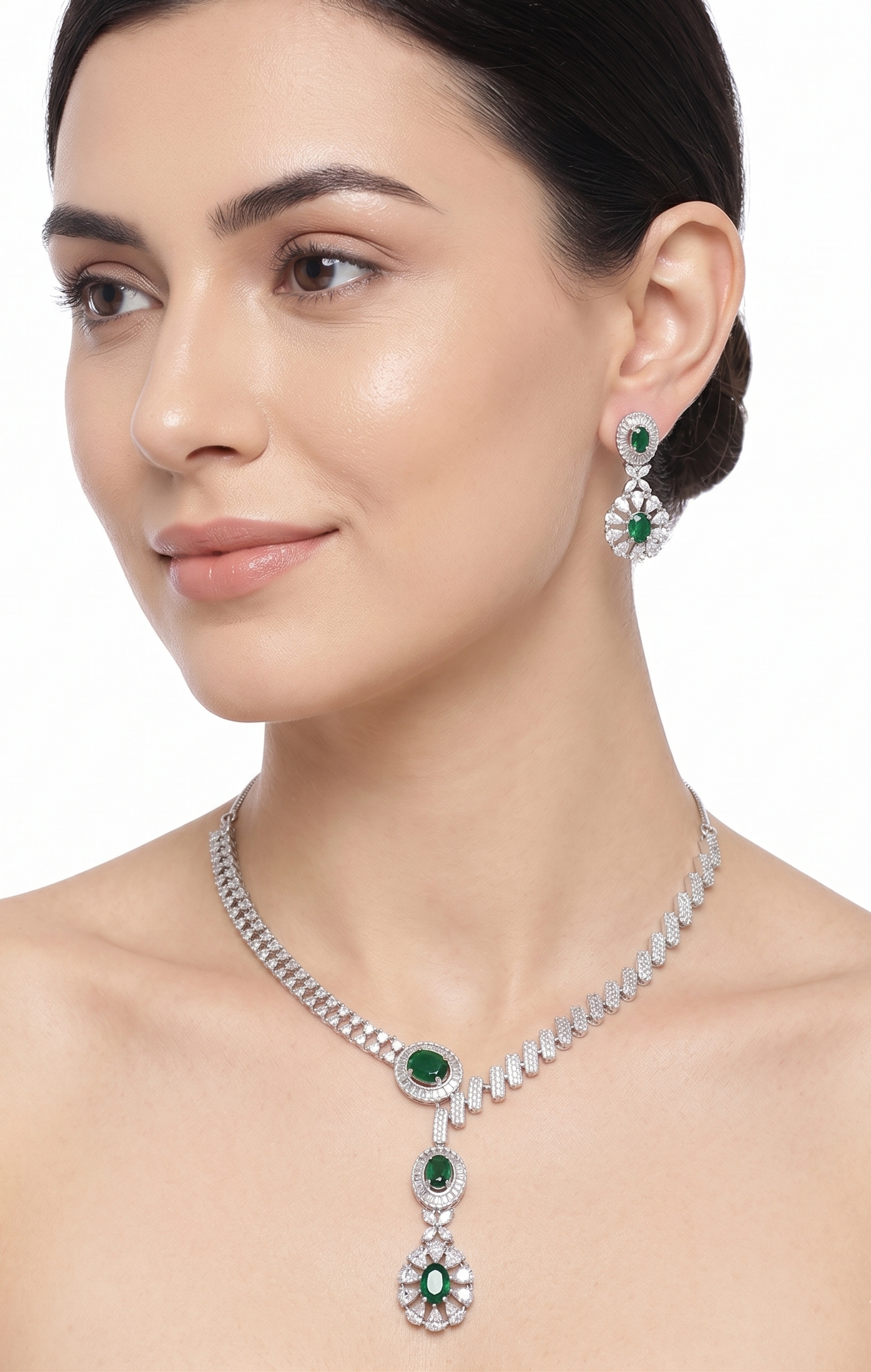 Woman wearing a silver necklace and earrings with green gemstones on a white background