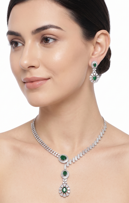 Woman wearing a silver necklace and earrings with green gemstones on a white background